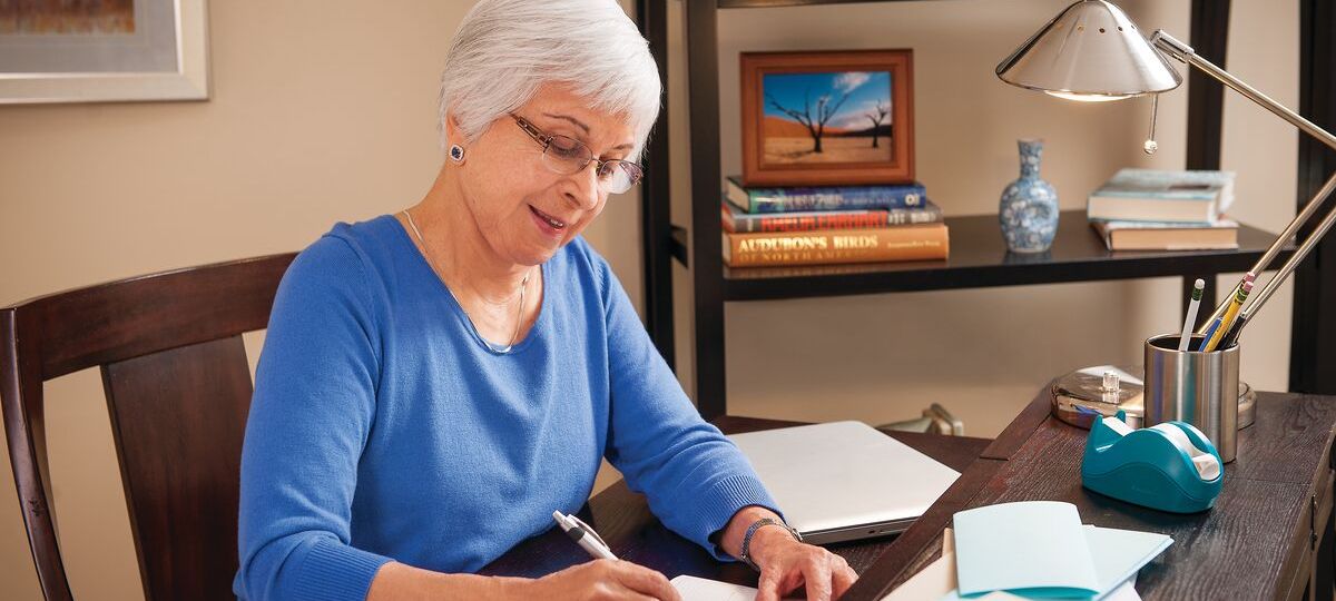 A woman sits at her desk with paperwork and bills