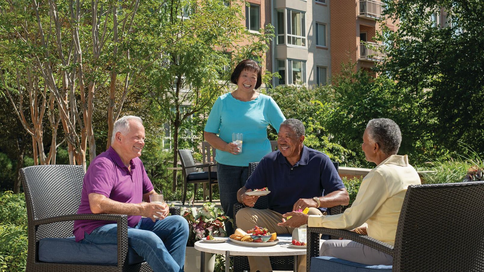 A diverse group of residents gather outside talking and laughing in an Erickson community courtyard.